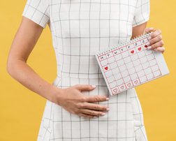 vrouw in witte jurk met hand op buik en kalender in hand middenboven