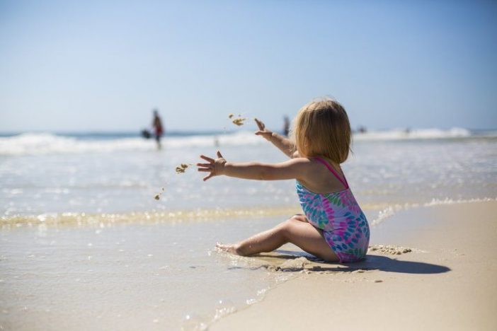 Klein meisje zit in het zand aan zee